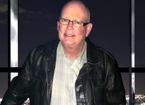 Smiling Doctor White is shown above in a photo on vacation in a leather jacket with a night sky background