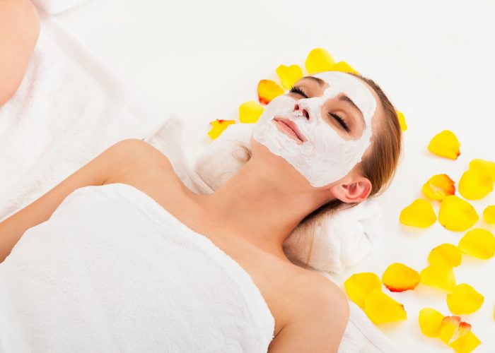 Women with a face mask, laying down with yellow petals around her in a towel